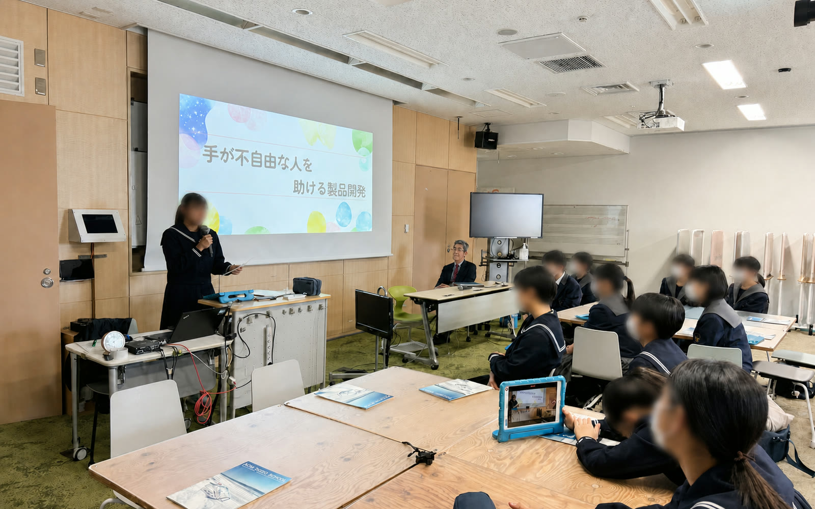 楢葉中学校の総合学習で発表する生徒と見守る岸博幸（生徒の顔はぼかし処理済み）