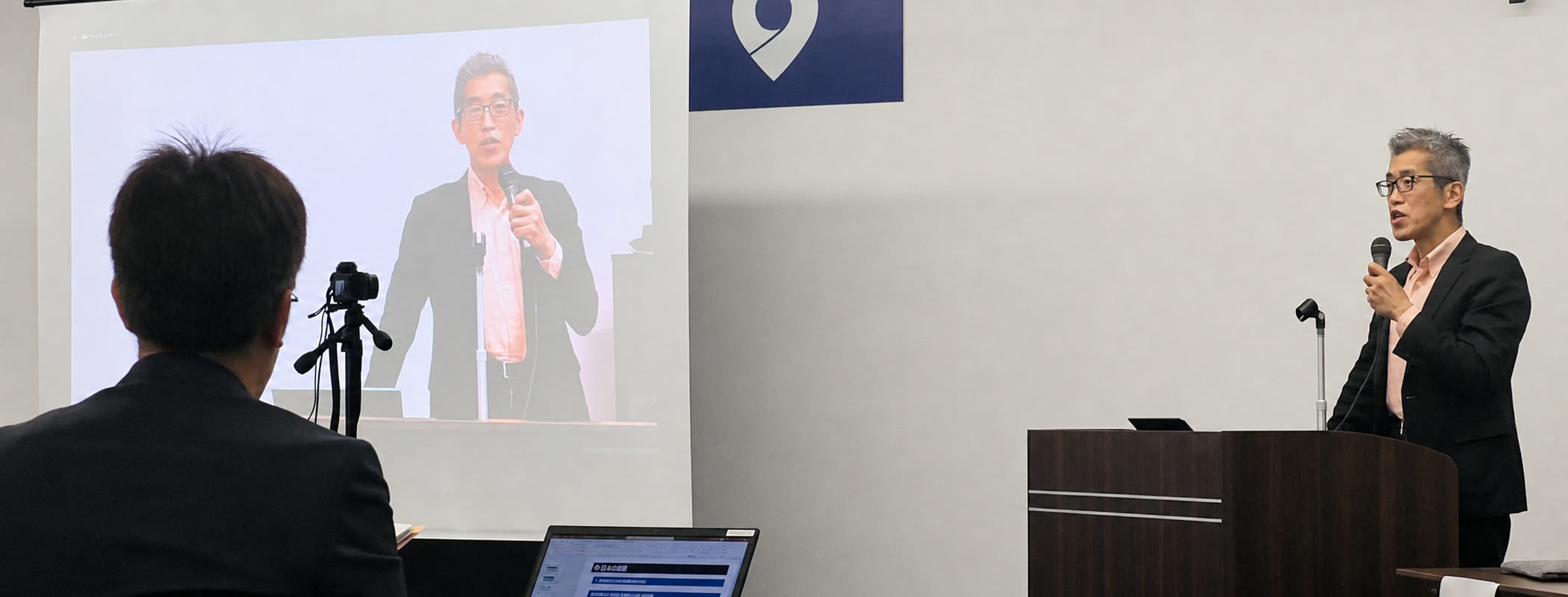 講演会場で登壇し、マイクを持って話す岸博幸